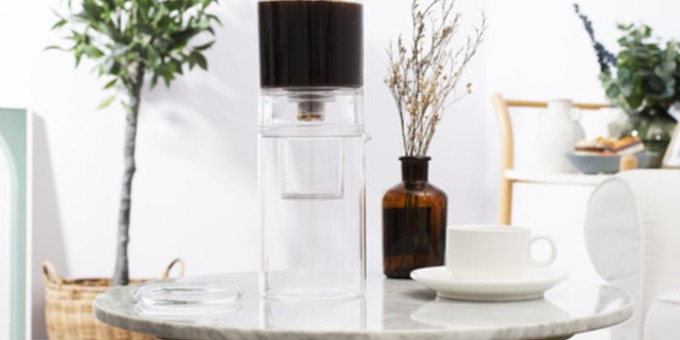 Dripster auf weißem Marmortisch neben Kaffeetasse und Vase, im Hintergrund zwei Pflanzen