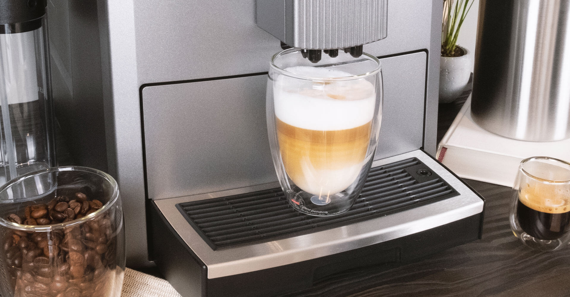 Kaffeespezialitäten wie ein Espresso oder Latte Macchiato stehen auf dem Tisch, daneben ein grauer Vollautomat