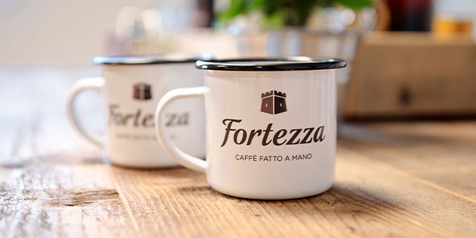Zwei weiße Emaille Becher auf Holztisch mit braunem Fortezza Logo