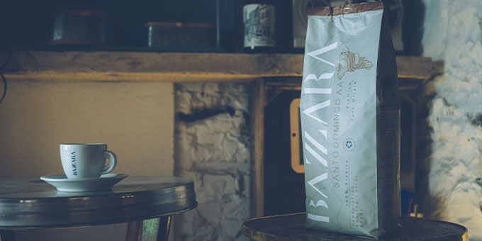 Hellgraue Bazzara Kaffeeverpackung mit Cappuccinotasse auf Holztisch in robuster Landhausküche