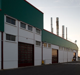Grün/weißes Produktionsgebäude  von außen beim Sonnenuntergang